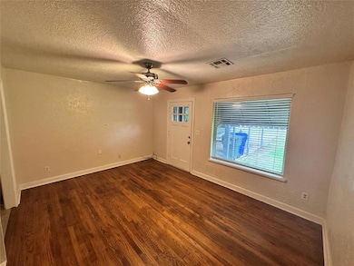 Empty room with dark wood-type flooring, a textured ceiling, a ceiling fan, a textured wall, and baseboards