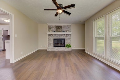 Unfurnished living room with a textured ceiling, dark wood-style floors, a ceiling fan, and a fireplace