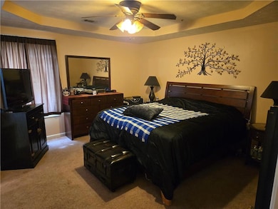 Bedroom featuring a tray ceiling, light colored carpet, ceiling fan, and a textured ceiling