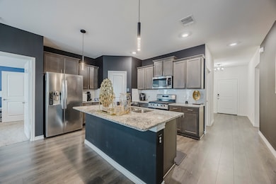Kitchen with stainless steel appliances, tasteful backsplash, light stone countertops, a kitchen island with sink, and hanging light fixtures