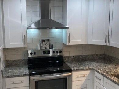 Kitchen with stainless steel electric stove, wall chimney exhaust hood, white cabinets, backsplash, and stone countertops