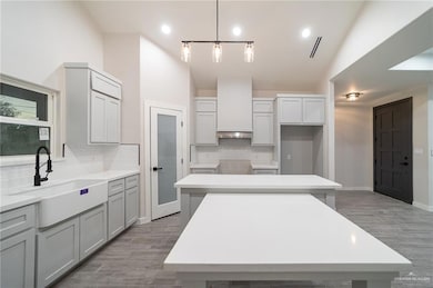 Kitchen with backsplash, hanging light fixtures, wood finished floors, a center island, and high vaulted ceiling