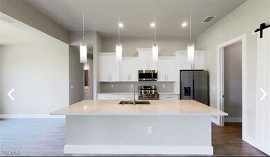 Kitchen featuring appliances with stainless steel finishes, white cabinets, an island with sink, decorative light fixtures, and recessed lighting