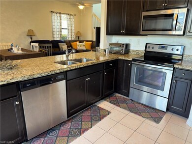 Kitchen with stainless steel appliances, open floor plan, light tile patterned floors, light stone counters, and a ceiling fan