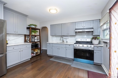Kitchen with appliances with stainless steel finishes, decorative backsplash, dark wood-style flooring, arched walkways, and under cabinet range hood