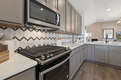 Kitchen featuring appliances with stainless steel finishes, vaulted ceiling, dark wood-style floors, gray cabinets, and light stone countertops