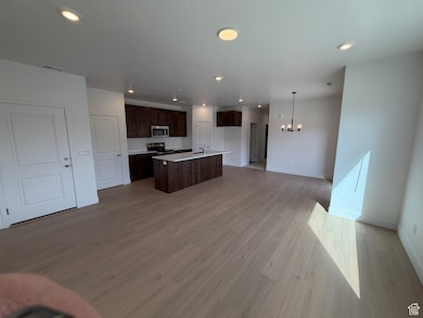 Kitchen featuring open floor plan, light countertops, dark brown cabinets, a kitchen island with sink, and light wood-style flooring
