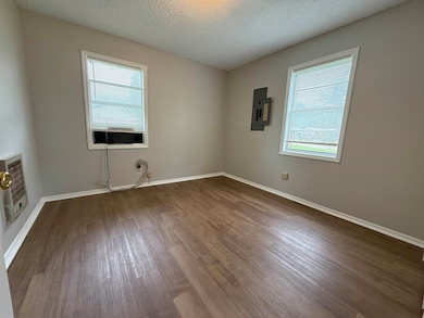 Empty room with wood finished floors, heating unit, electric panel, and baseboards