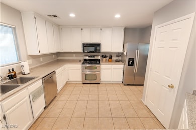 Kitchen featuring stainless steel appliances, white cabinetry, light tile patterned floors, recessed lighting, and light stone counters