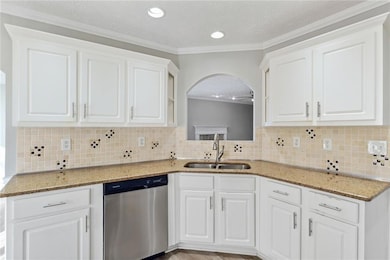 Kitchen with dishwasher, white cabinets, light stone countertops, arched walkways, and tasteful backsplash
