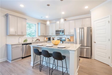 Kitchen featuring appliances with stainless steel finishes, a kitchen breakfast bar, a center island, light wood-style floors, and ornamental molding
