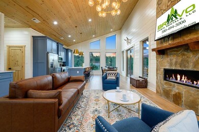 Living room featuring high vaulted ceiling, wood finished floors, recessed lighting, wood walls, and a stone fireplace
