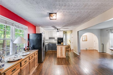Kitchen featuring stainless steel refrigerator with ice dispenser, a textured ceiling, arched walkways, a ceiling fan, and dark wood-style floors