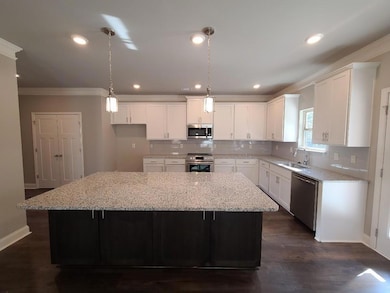 Kitchen featuring ornamental molding, hanging light fixtures, white cabinetry, light stone countertops, and a kitchen island