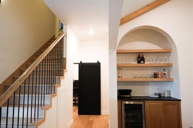 Indoor dry bar with wine cooler, light wood-style flooring, stairway, and a barn door