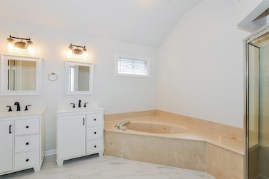 Full bathroom featuring lofted ceiling, a bath, two vanities, marble finish floors, and a shower with door