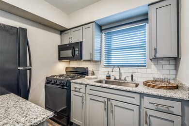 Kitchen featuring black appliances, tasteful backsplash, light stone counters, and gray cabinetry