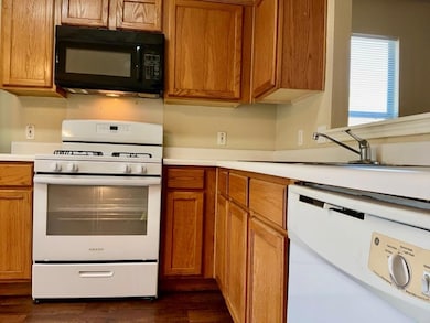 Kitchen with white appliances, light countertops, brown cabinetry, and dark wood finished floors