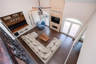 Living room with a high ceiling, dark wood-type flooring, ceiling fan, and a brick fireplace