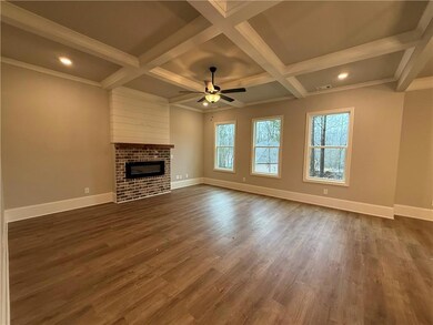 Living room featuring brick fireplace with shiplap above the mantel, ceiling fan, baseboards, coffered ceiling, and with healthy amount of natural light.