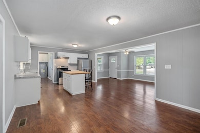 Kitchen with stainless steel range with electric stovetop, butcher block counters, white cabinetry, dark wood-style floors, and water heater