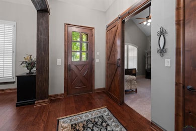 Foyer entrance with a barn door, dark wood-type flooring, a ceiling fan, and vaulted ceiling