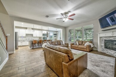 Living room with light wood-type flooring, ceiling fan, a textured ceiling, a stone fireplace, and stairway