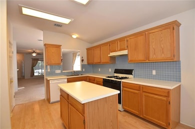 Kitchen featuring gas stove, tasteful backsplash, lofted ceiling, light countertops, and light wood finished floors