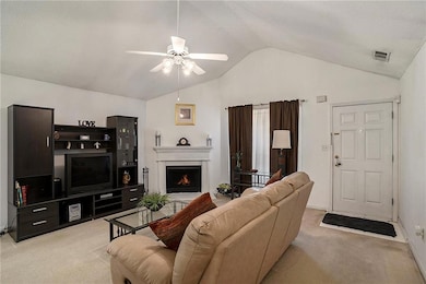 Living area featuring light carpet, vaulted ceiling, a ceiling fan, a lit fireplace, and baseboards