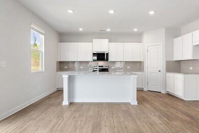 Kitchen featuring stainless steel appliances, backsplash, a center island with sink, light wood-style floors, and white cabinetry