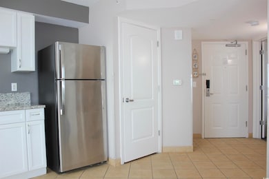 Kitchen featuring white cabinetry, light stone countertops, light tile patterned floors, and stainless steel refrigerator