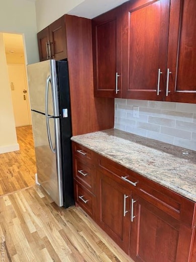 Kitchen with refrigerator, light wood-style flooring, light stone countertops, and reddish brown cabinets