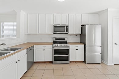 Kitchen featuring appliances with stainless steel finishes, ornamental molding, white cabinets, light countertops, and light tile patterned flooring