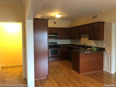 Kitchen with stainless steel appliances, ornamental molding, light wood finished floors, dark brown cabinets, and a peninsula