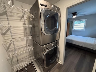 Walk-in-closet with built-in Laundry room featuring stacked washing machine and dryer, wood finished floors, and ceiling fan