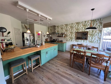 Kitchen with wooden counters, wallpapered walls, appliances with stainless steel finishes, wood finished floors, and blue cabinets
