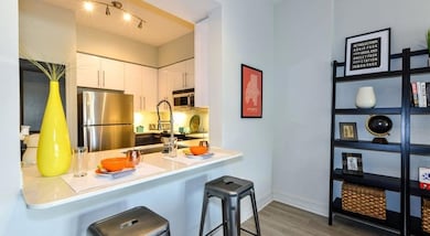 Kitchen featuring stainless steel appliances, rail lighting, white cabinets, hardwood / wood-style floors, and a breakfast bar