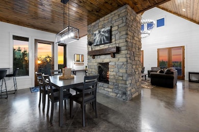 Dining room featuring an outdoor stone fireplace, a chandelier, finished concrete flooring, wooden walls, and french doors