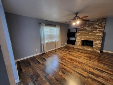 Unfurnished living room with a brick fireplace, dark wood finished floors, and a ceiling fan
