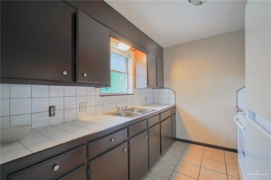 Kitchen featuring backsplash, a sink, baseboards, tile counters, and light tile patterned flooring