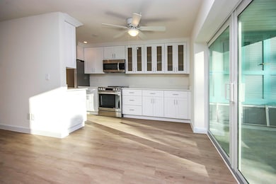 Kitchen with appliances with stainless steel finishes, ceiling fan, white cabinets, light wood-type flooring, and glass insert cabinets