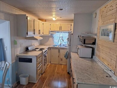 Kitchen featuring light countertops, light wood-type flooring, white appliances, a textured ceiling, and wooden walls