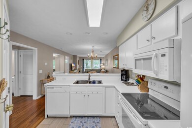Kitchen with white appliances, a peninsula, a chandelier, open floor plan, and white cabinetry