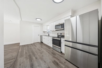 Kitchen featuring appliances with stainless steel finishes, white cabinets, tasteful backsplash, and light wood-type flooring