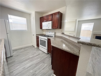 Kitchen with white appliances, light wood finished floors, light stone counters, and a textured ceiling