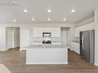 Kitchen featuring white cabinetry, appliances with stainless steel finishes, light wood-style floors, recessed lighting, and light stone counters