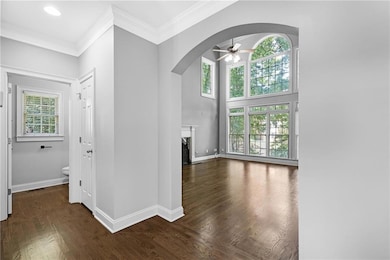 Unfurnished living room featuring arched walkways, ceiling fan, a high end fireplace, dark wood-style flooring, and crown molding