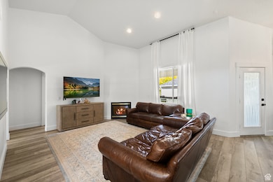 Living room featuring a glass covered fireplace, light wood-style flooring, recessed lighting, high vaulted ceiling, and arched walkways