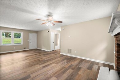 Unfurnished living room featuring a brick fireplace, ceiling fan, wood finished floors, and a textured ceiling