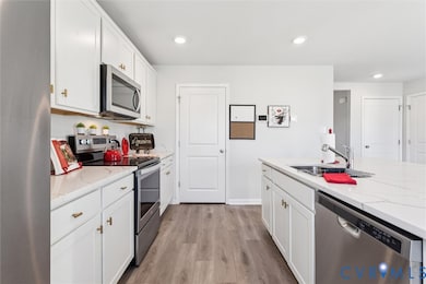 Kitchen featuring stainless steel appliances, white cabinetry, recessed lighting, light wood-style floors, and light stone counters